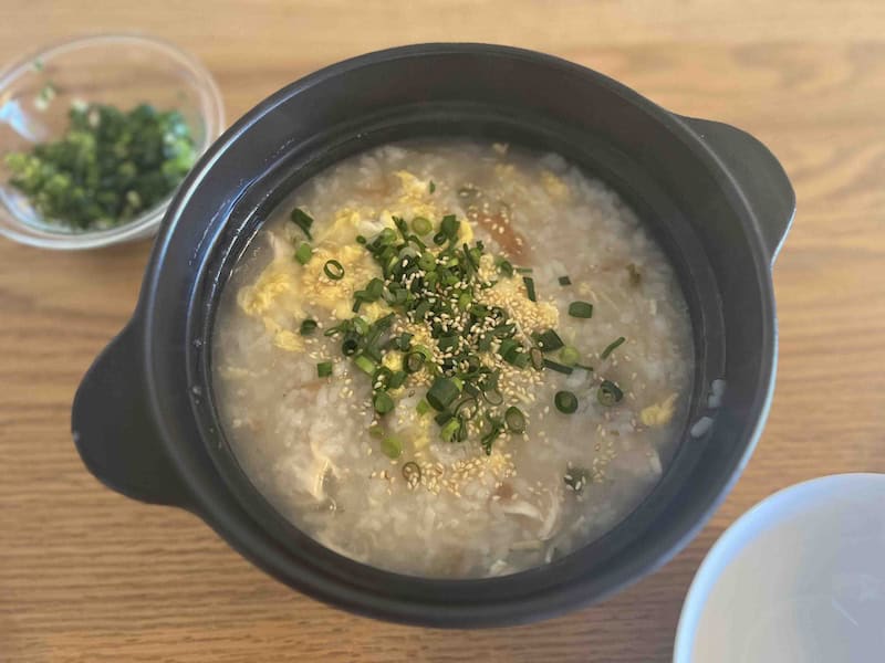 土鍋で作った鶏ささみ・生姜・梅干し入りの卵とじ和風粥に小ネギと胡麻があしらわれている